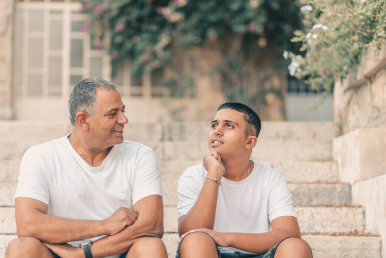 Teen boy sitting next to father on steps outside